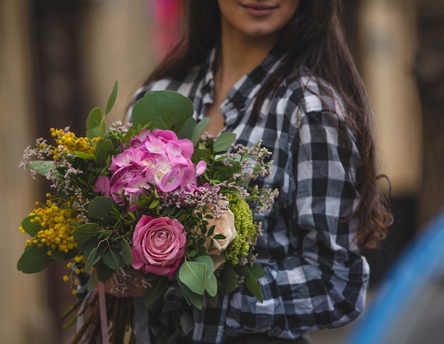 Una mujer sosteniendo un ramo de flores mixtas en tonos de rosa en la mano en una vista de la calle