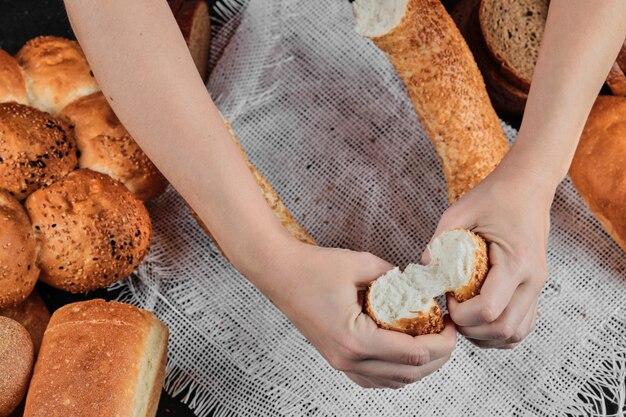 Mujer sosteniendo rebanadas de bagel sobre mesa oscura con varios panes