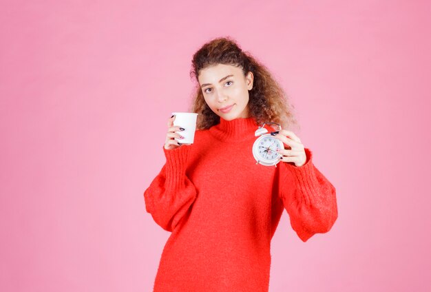 mujer sosteniendo un reloj despertador y una taza de café apuntando a su rutina matutina.