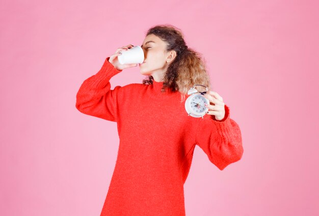 mujer sosteniendo un reloj despertador y tomando café.