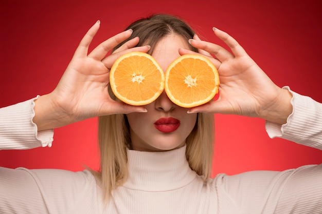 Foto gratuita mujer sosteniendo rodajas de naranja sobre sus ojos