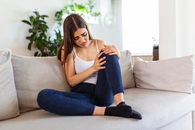 Mujer sosteniendo la rodilla con dolor en el sofá. Atención médica y concepto médico.