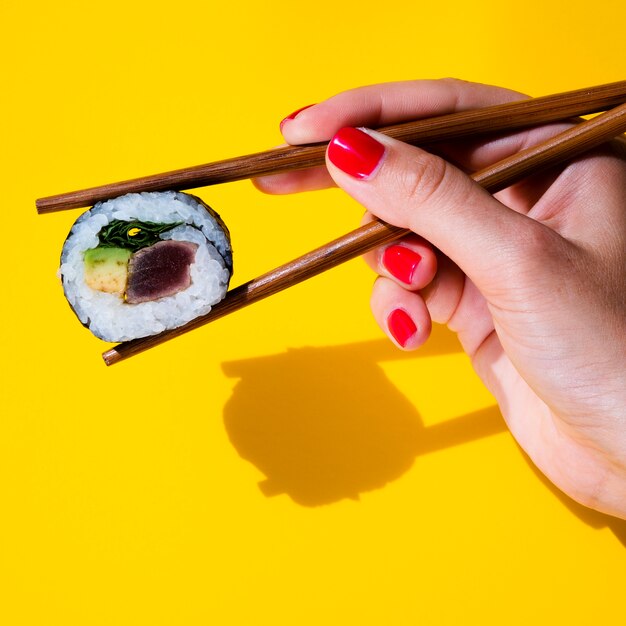 Mujer sosteniendo un rollo de sushi en palillos sobre fondo amarillo