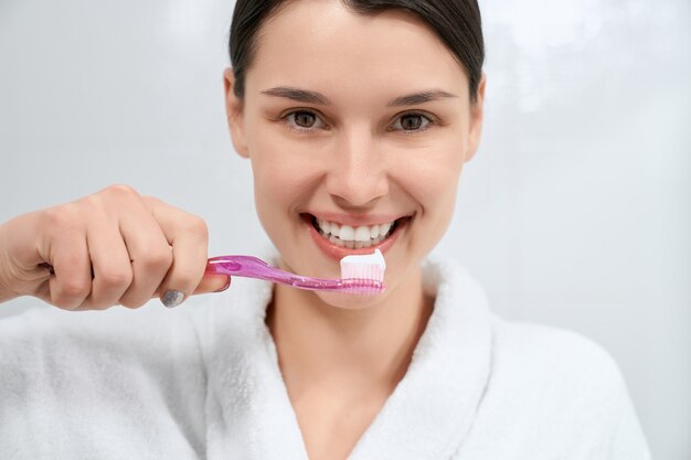 Mujer sosteniendo rosa cepillo de dientes con pasta de dientes en el baño.