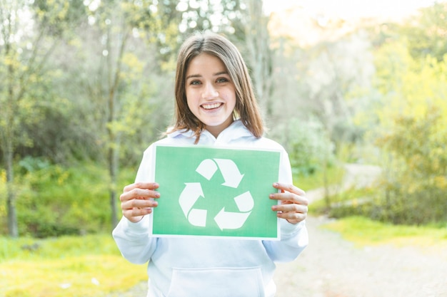 Mujer sosteniendo el símbolo de reciclaje en el bosque