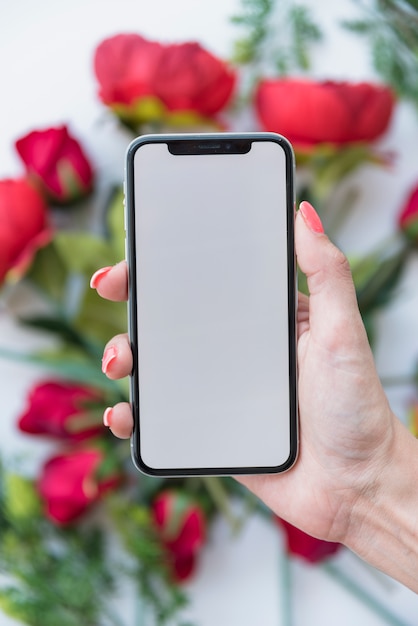 Foto gratuita mujer sosteniendo smartphone con pantalla en blanco sobre rosas rojas