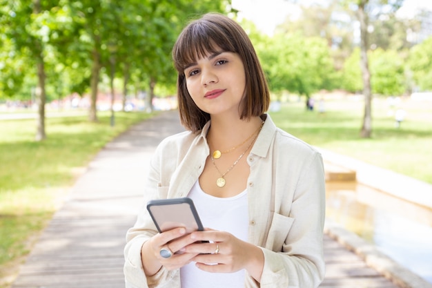 Mujer sosteniendo smartphone y sonriendo en el parque