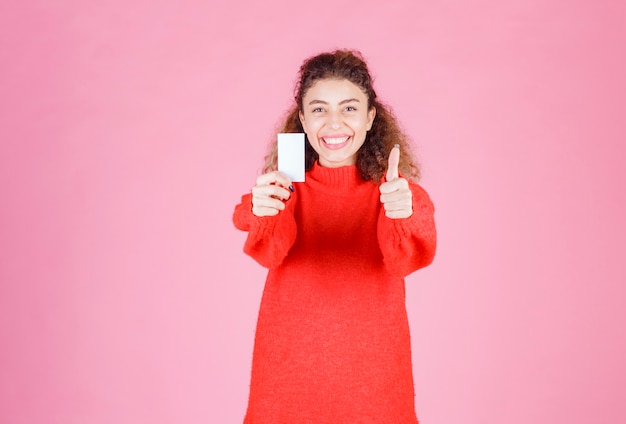 mujer sosteniendo su nueva tarjeta de visita y mostrando el signo de la mano de disfrute.