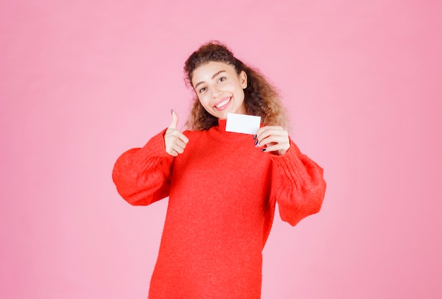 mujer sosteniendo su nueva tarjeta de visita y mostrando el signo de la mano de disfrute.