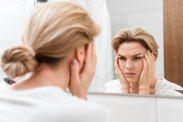 Mujer sosteniendo su rostro y mirándose en el espejo