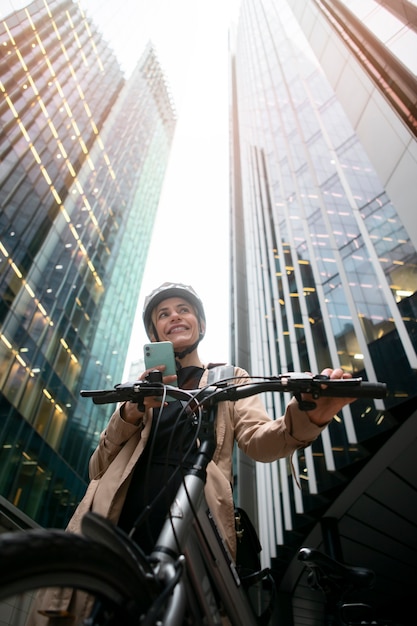Mujer sosteniendo su teléfono inteligente y caminando en su bicicleta