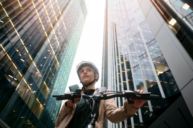 Mujer sosteniendo su teléfono inteligente y caminando en su bicicleta