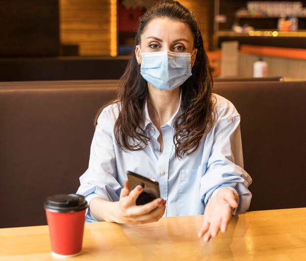 Mujer sosteniendo su teléfono mientras usa una máscara facial