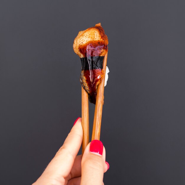 Mujer sosteniendo un sushi sobre un fondo gris