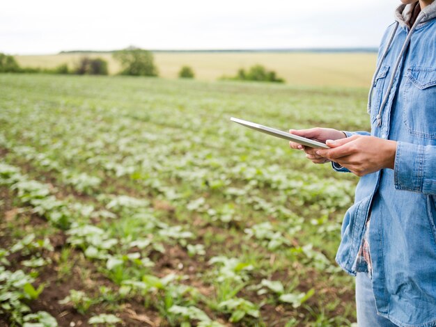 Mujer sosteniendo una tableta junto a un campo agrícola con espacio de copia