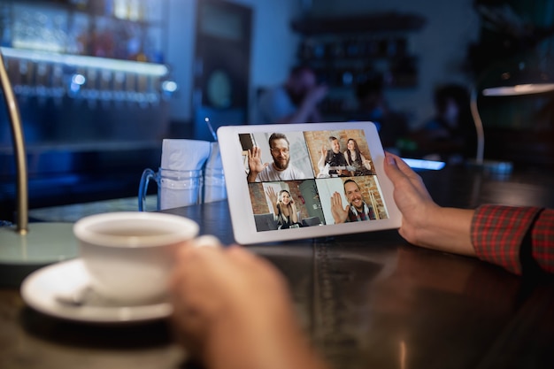 Mujer sosteniendo una tableta para videollamada mientras bebe café