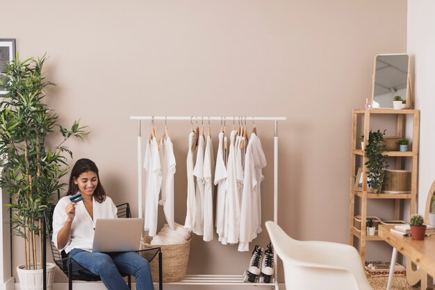 Mujer sosteniendo una tarjeta de crédito y trabajando en la computadora portátil