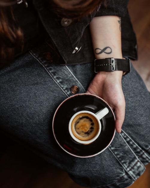Mujer sosteniendo una taza de café espresso en sus piernas