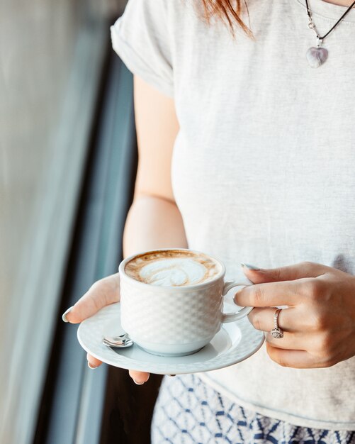 Mujer sosteniendo una taza de café frente a la ventana