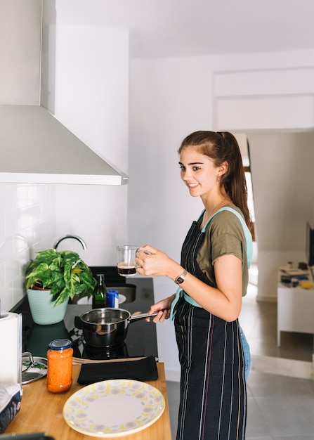 Foto gratuita mujer sosteniendo la taza de café en la mano preparando la comida en la cocina