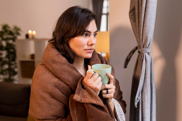 Mujer sosteniendo una taza de café mientras está cubierto con una manta