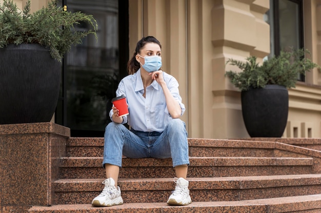 Mujer sosteniendo una taza de café mientras está sentado en las escaleras con espacio de copia