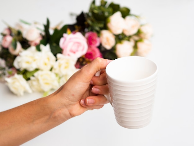 Foto gratuita mujer sosteniendo una taza con un ramo de rosas en el fondo