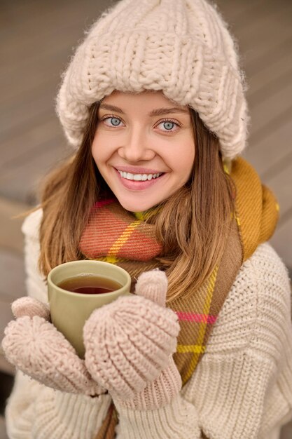 Mujer sosteniendo taza sonriendo a la cámara al aire libre