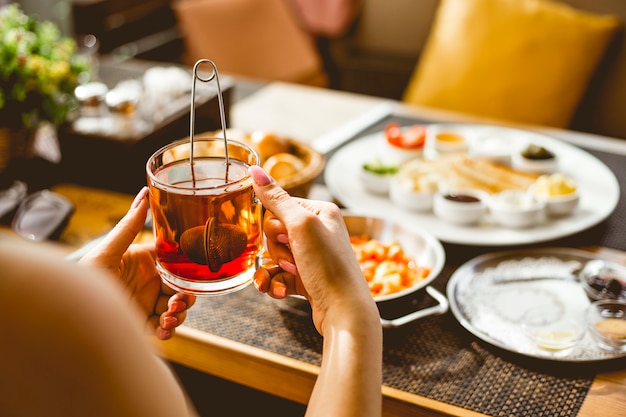 Una mujer sosteniendo una taza de té negro y desayuno en la mesa