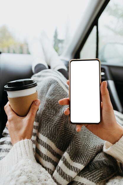 Mujer sosteniendo un teléfono en blanco y una taza de café
