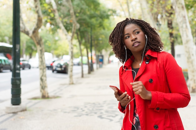 Mujer sosteniendo teléfono inteligente y mirando hacia el lado en la calle