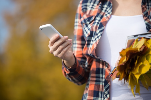 Mujer sosteniendo el teléfono en la mano, hojas amarillas en otro