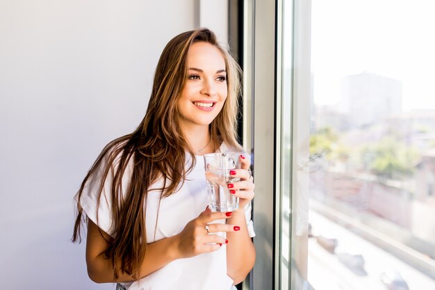 Mujer sosteniendo un vaso de agua mientras mira por la ventana - parte posterior de la silueta de la mujer