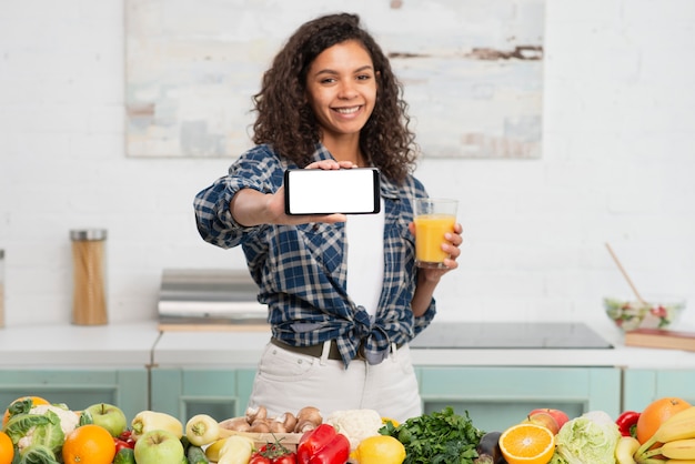 Mujer sosteniendo un vaso de jugo y mostrando teléfono simulacro