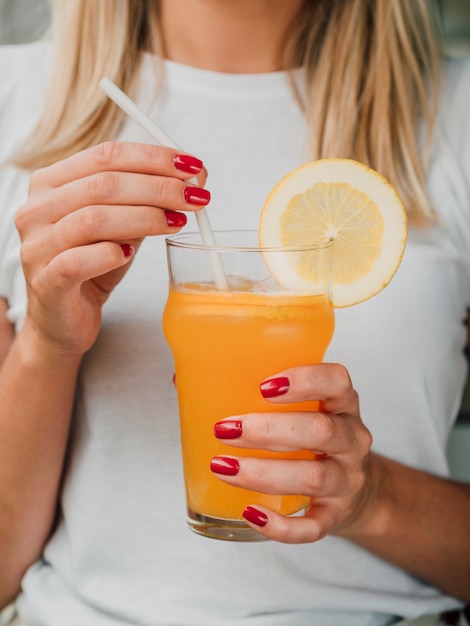 Mujer sosteniendo un vaso de jugo de naranja y paja