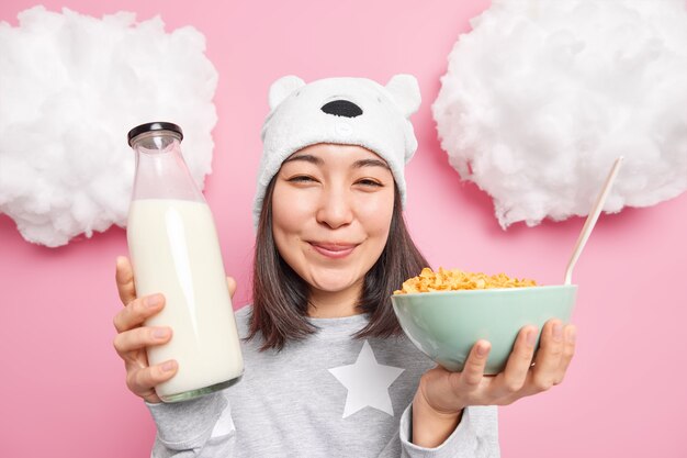 Mujer sostiene una botella de leche y copos de maíz vestida con un pijama informal que va a desayunar después de despertar disfruta del comienzo del nuevo día