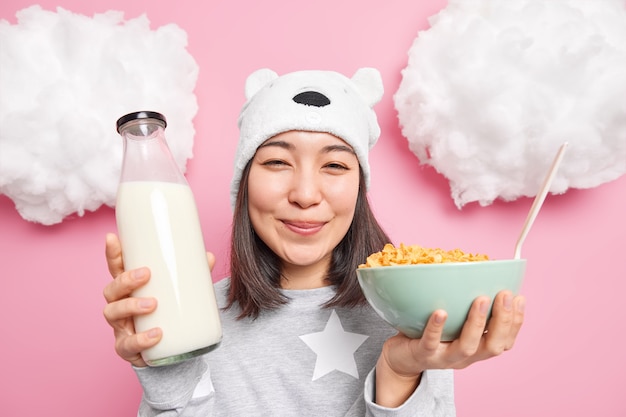 Mujer sostiene una botella de leche y copos de maíz vestida con un pijama informal que va a desayunar después de despertar disfruta del comienzo del nuevo día