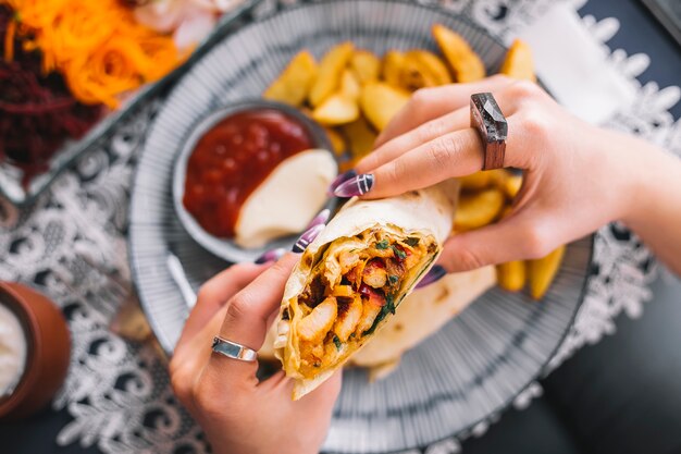 Mujer sostiene burrito de pollo servido con papas fritas y salsas