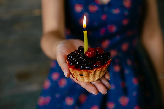 La mujer sostiene un cupcake de fruta con vela. Vista de primer plano.