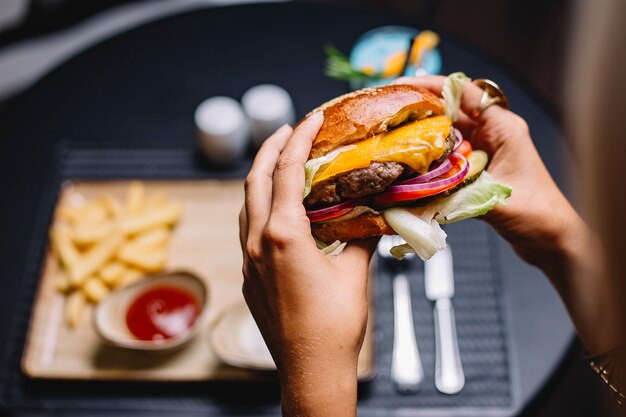 Mujer sostiene hamburguesa de ternera con lechuga tomate cebolla roja y queso cheddar