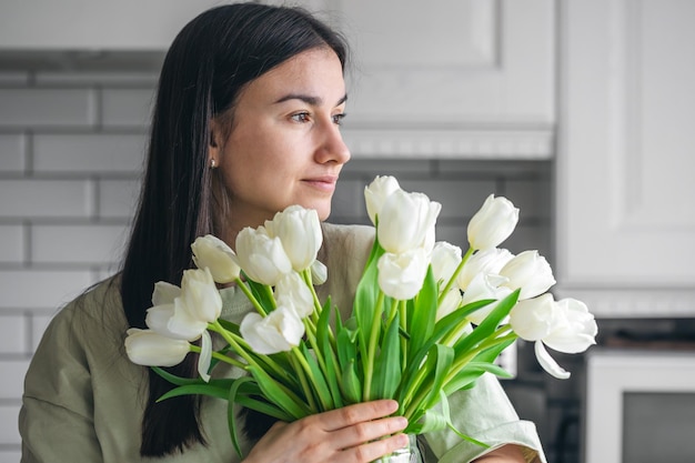 Foto gratuita una mujer sostiene un jarrón con tulipanes blancos en un interior de la cocina