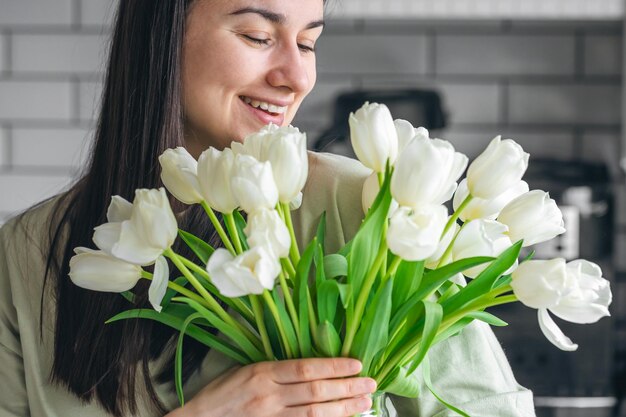 Una mujer sostiene un jarrón con tulipanes blancos en un interior de la cocina