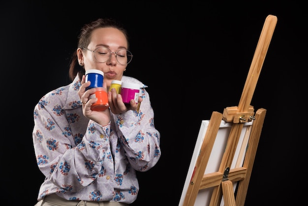 Foto gratuita mujer sostiene pincel y pinturas sobre fondo negro