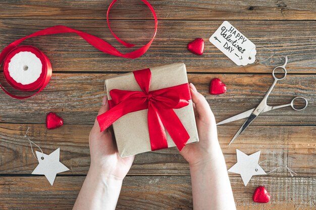 Una mujer sostiene un regalo envuelto para el día de San Valentín en un fondo de madera