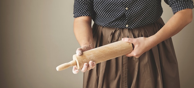 La mujer sostiene el rodillo de madera en las manos y lo frota con harina