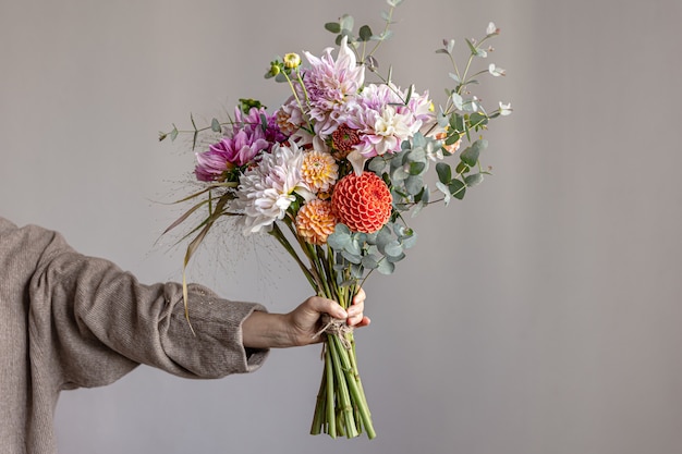 Una mujer sostiene en su mano un arreglo floral festivo con brillantes flores de crisantemo, un ramo festivo.