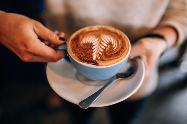 La mujer sostiene la taza en el platillo con café con leche caliente