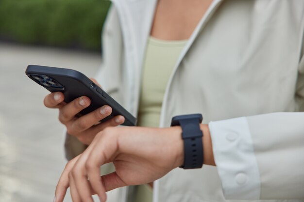 La mujer sostiene un teléfono inteligente moderno y un reloj inteligente portátil que usa una aplicación de fitness en un dispositivo portátil para monitorear el rendimiento del entrenamiento.