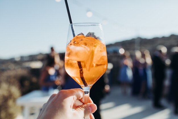 Mujer sostiene un vaso con bebida de naranja con cubitos de hielo contra el sol