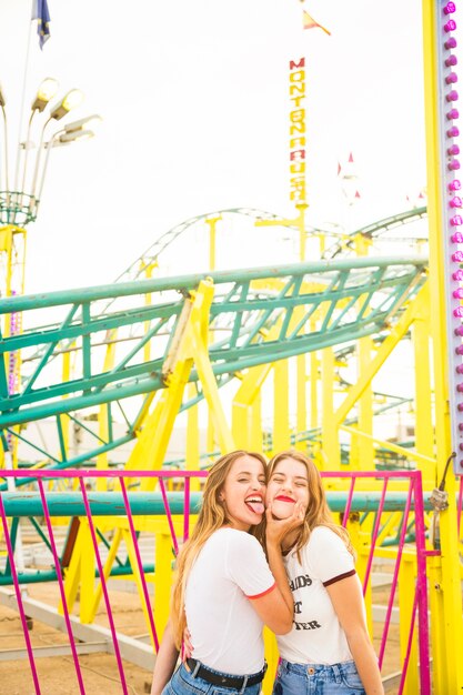 Mujer con su amiga sacando la lengua delante de la montaña rusa